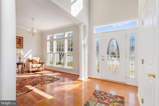 entryway featuring light hardwood / wood-style flooring, a notable chandelier, a towering ceiling, crown molding, and decorative columns