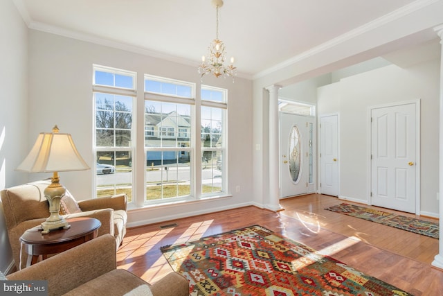 entrance foyer featuring decorative columns, crown molding, light wood-type flooring, and an inviting chandelier