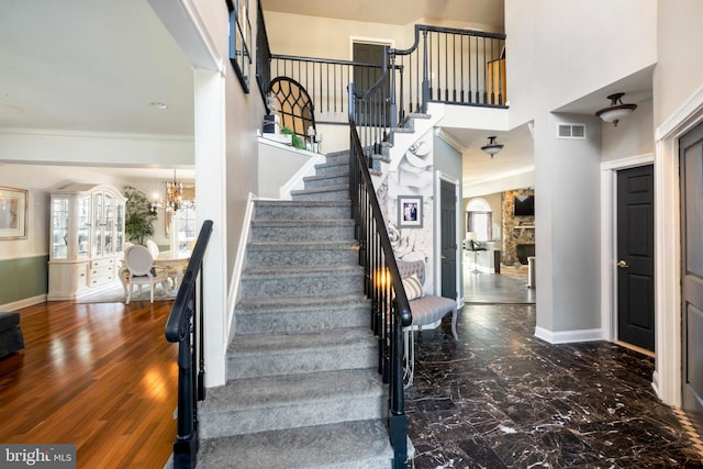 staircase featuring hardwood / wood-style flooring, a stone fireplace, a high ceiling, and a notable chandelier