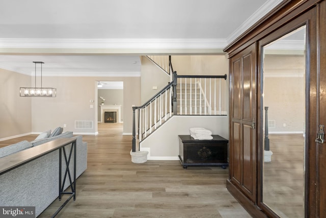 entryway featuring a warm lit fireplace, light wood-style flooring, stairway, and visible vents