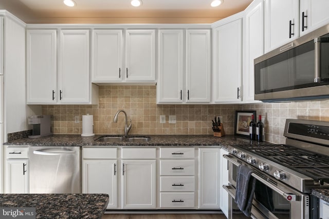 kitchen with stainless steel appliances, backsplash, white cabinetry, a sink, and dark stone counters