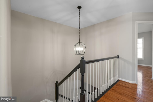 stairway with an inviting chandelier, baseboards, and wood finished floors