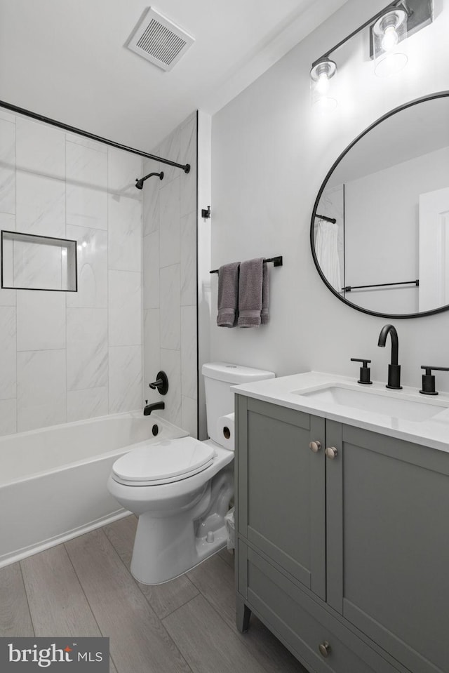 bathroom featuring toilet, wood finish floors, vanity, visible vents, and tub / shower combination