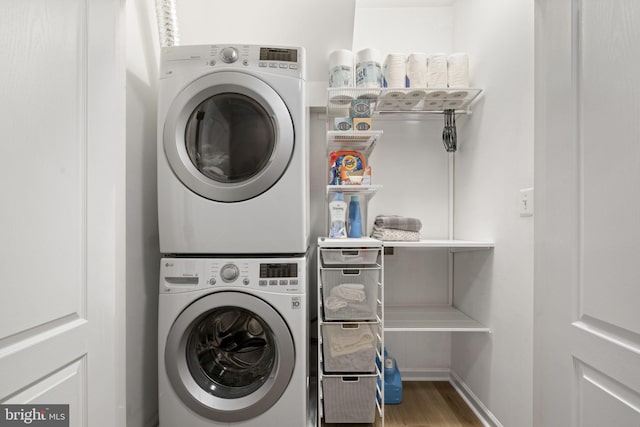 laundry area featuring laundry area, stacked washer / dryer, wood finished floors, and baseboards