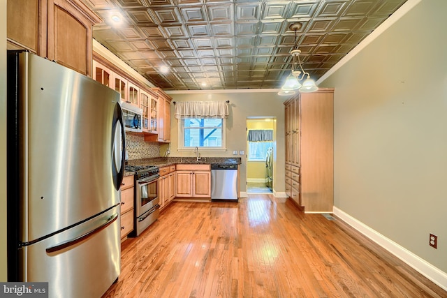 kitchen with a sink, baseboards, appliances with stainless steel finishes, light wood finished floors, and an ornate ceiling