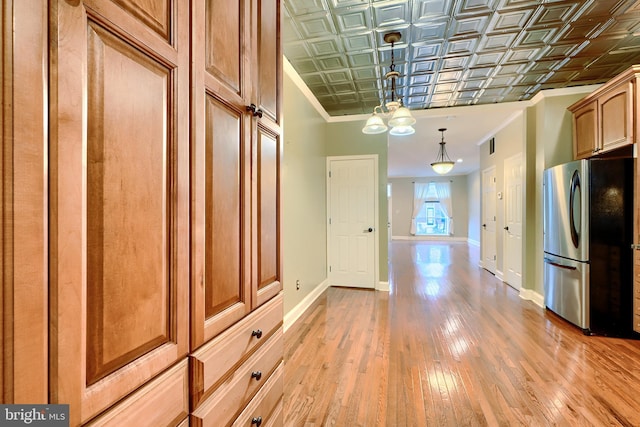 kitchen with an ornate ceiling, ornamental molding, freestanding refrigerator, light wood-type flooring, and baseboards