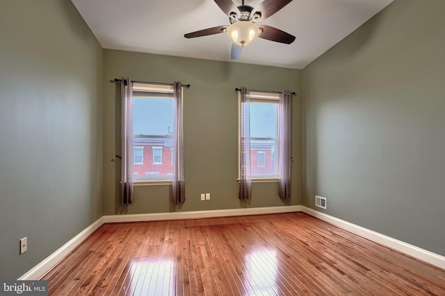 unfurnished room with hardwood / wood-style flooring, visible vents, baseboards, and ceiling fan