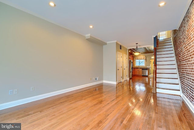 unfurnished living room with brick wall, baseboards, stairway, light wood finished floors, and crown molding