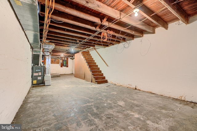 unfinished below grade area featuring electric panel, heating unit, and stairs