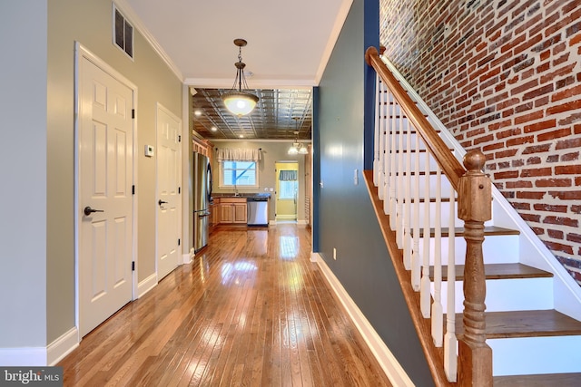 foyer entrance with visible vents, baseboards, ornamental molding, stairway, and wood-type flooring