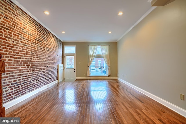 unfurnished living room featuring ornamental molding, wood-type flooring, baseboards, and brick wall