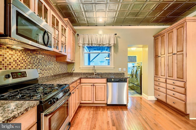 kitchen featuring an ornate ceiling, washing machine and clothes dryer, a sink, stainless steel appliances, and backsplash