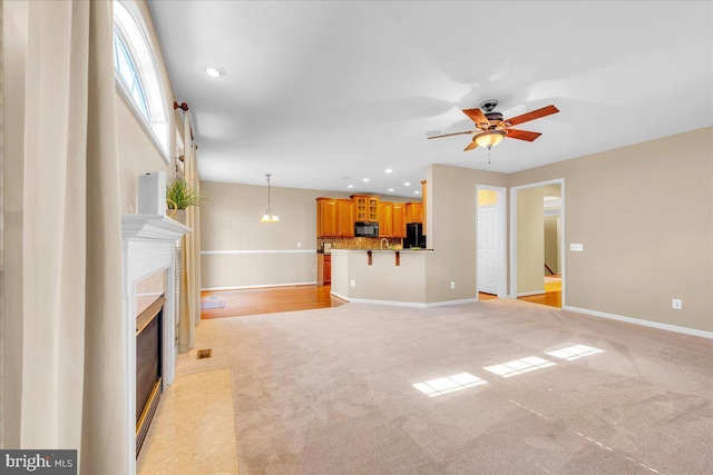 unfurnished living room with baseboards, light colored carpet, a fireplace with flush hearth, ceiling fan, and recessed lighting