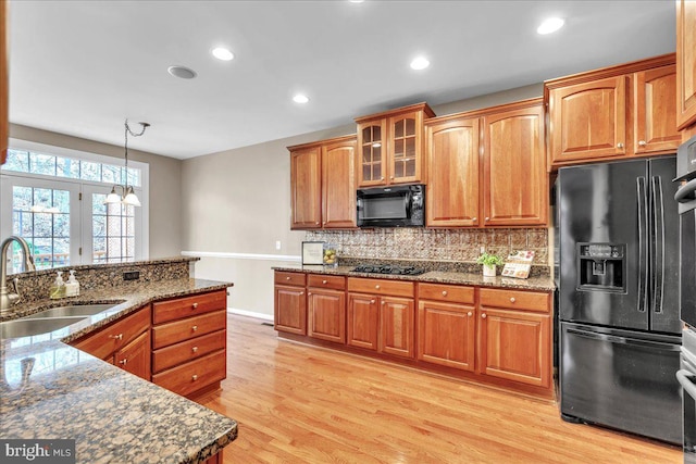 kitchen featuring a sink, light wood-style floors, black appliances, tasteful backsplash, and dark stone countertops