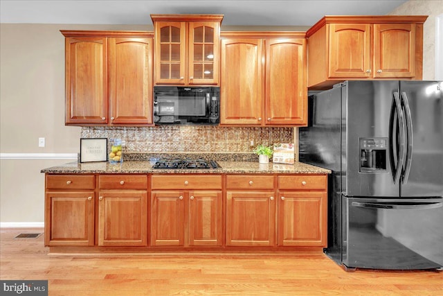 kitchen with black appliances, light stone counters, and light wood finished floors