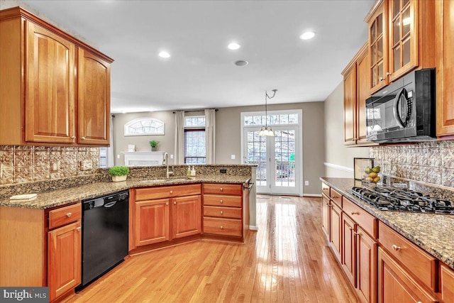 kitchen with stone countertops, light wood-style floors, a peninsula, black appliances, and a sink