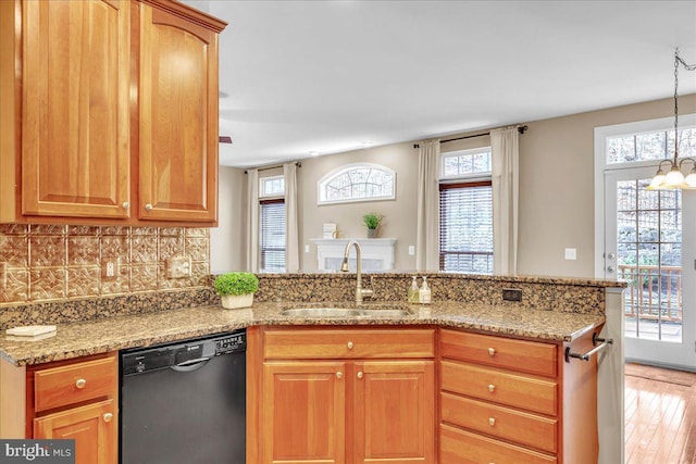 kitchen with black dishwasher, a peninsula, light stone countertops, a sink, and backsplash