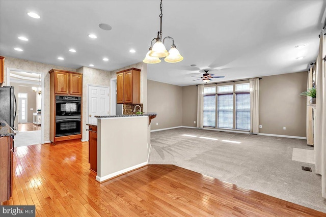 kitchen featuring dobule oven black, visible vents, dark stone countertops, freestanding refrigerator, and a peninsula