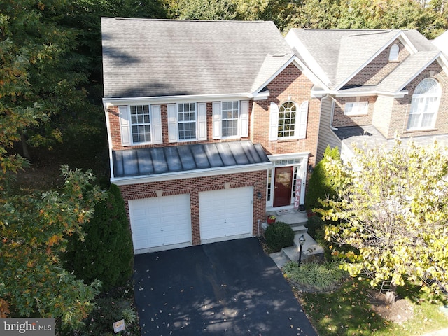 view of front of house with metal roof, aphalt driveway, a garage, brick siding, and a standing seam roof