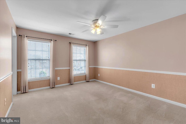 spare room featuring carpet, a wainscoted wall, visible vents, ceiling fan, and baseboards