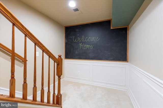 stairs with carpet floors, visible vents, and a decorative wall