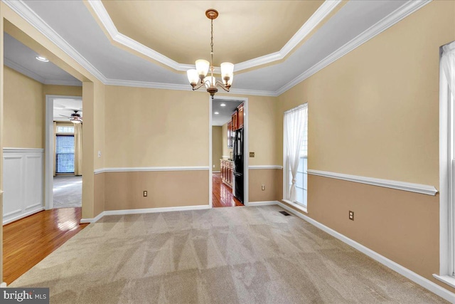 carpeted spare room with a chandelier, a tray ceiling, visible vents, and crown molding