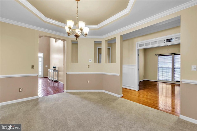 carpeted spare room featuring wood finished floors, ornamental molding, a raised ceiling, and a notable chandelier