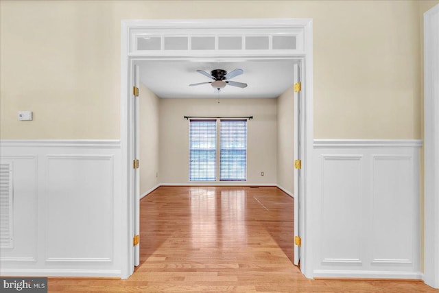 unfurnished room featuring a wainscoted wall, ceiling fan, and light wood finished floors