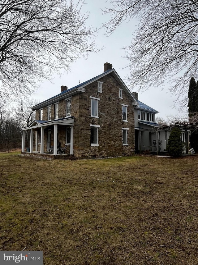 back of property with a yard, a chimney, and stone siding