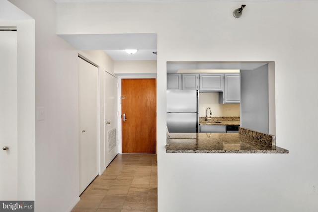 kitchen featuring a sink, dark stone countertops, stainless steel fridge, and gray cabinetry