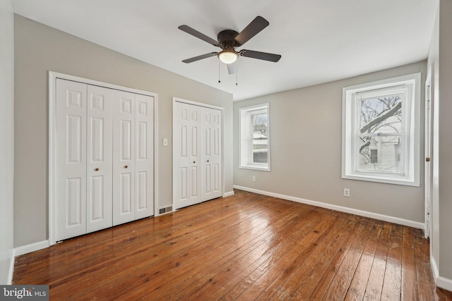 unfurnished bedroom featuring hardwood / wood-style flooring, ceiling fan, and two closets