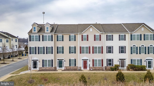 multi unit property featuring a residential view, stone siding, and a front yard