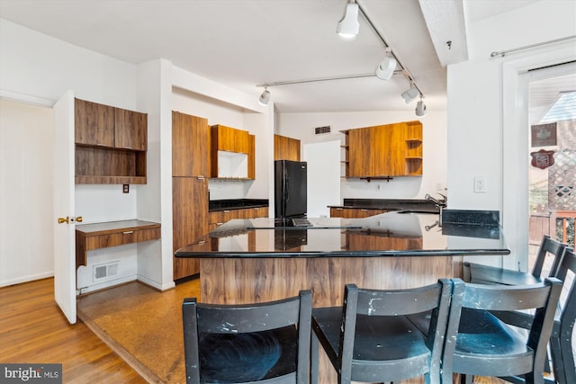 kitchen with open shelves, dark countertops, freestanding refrigerator, and brown cabinets