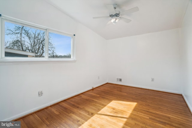 empty room with baseboards, visible vents, ceiling fan, wood finished floors, and vaulted ceiling