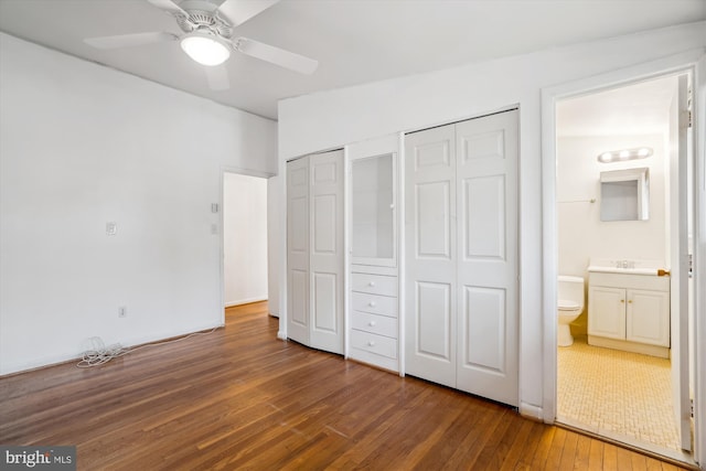 unfurnished bedroom featuring a ceiling fan, ensuite bath, hardwood / wood-style floors, two closets, and a sink