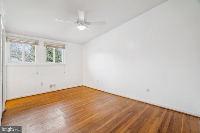 empty room featuring baseboards, visible vents, a ceiling fan, hardwood / wood-style flooring, and vaulted ceiling