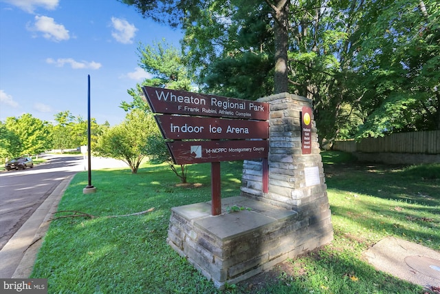 community / neighborhood sign featuring a yard and fence