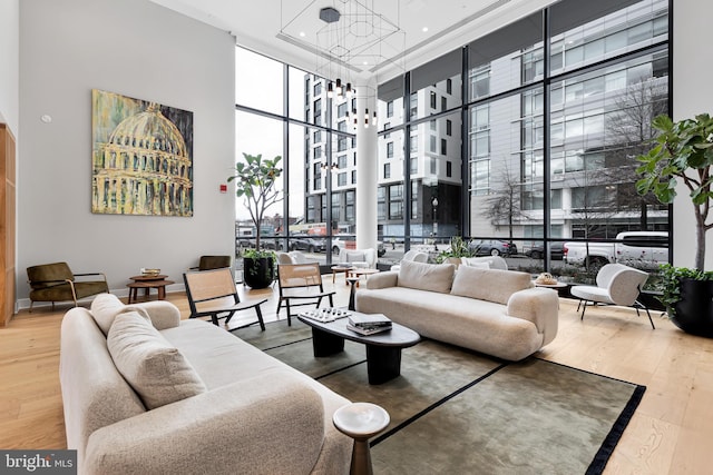 living room with a notable chandelier, wood-type flooring, floor to ceiling windows, and a towering ceiling