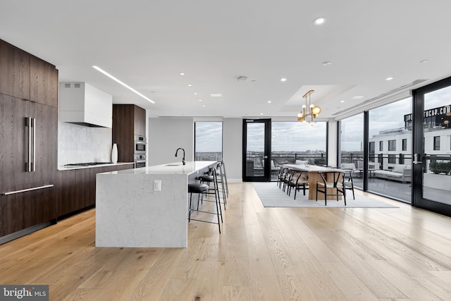 kitchen with appliances with stainless steel finishes, white cabinetry, light hardwood / wood-style floors, hanging light fixtures, and a kitchen island with sink