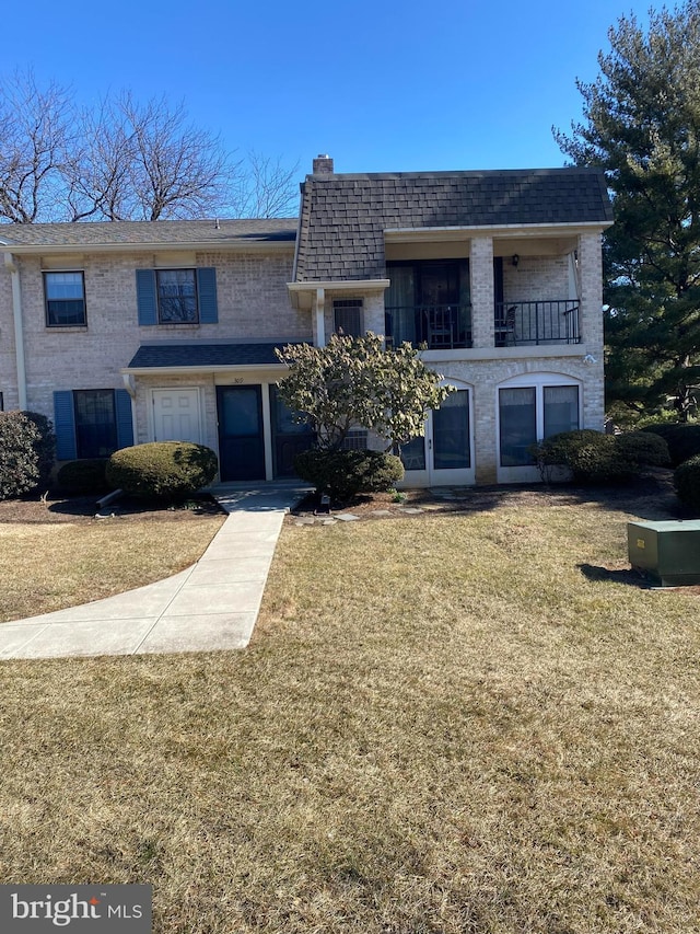 view of front facade featuring a front yard, brick siding, and a balcony