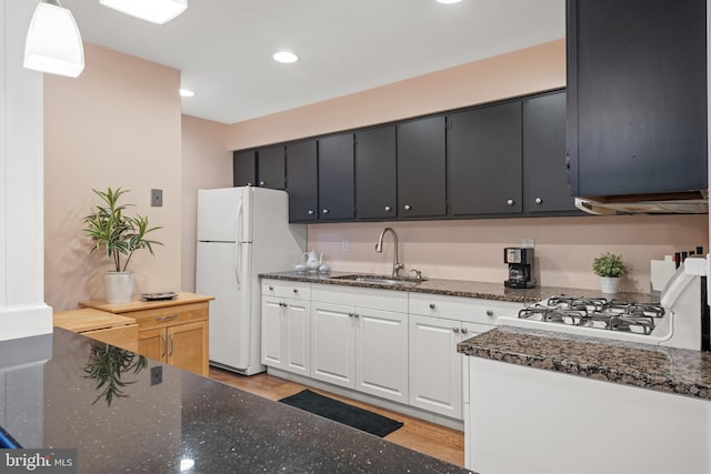 kitchen featuring recessed lighting, light wood-style flooring, freestanding refrigerator, a sink, and dark stone countertops