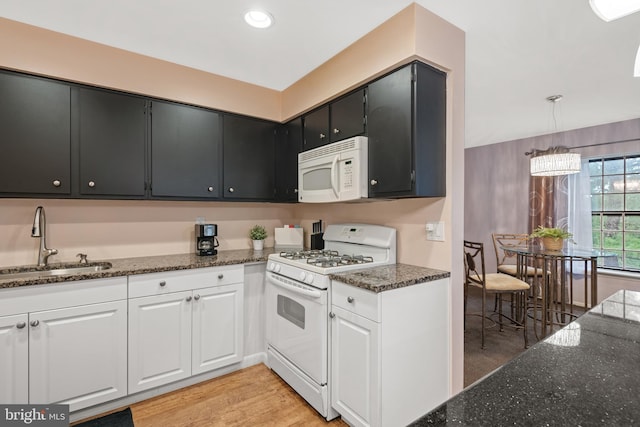 kitchen with dark stone counters, white appliances, a sink, and light wood-style flooring