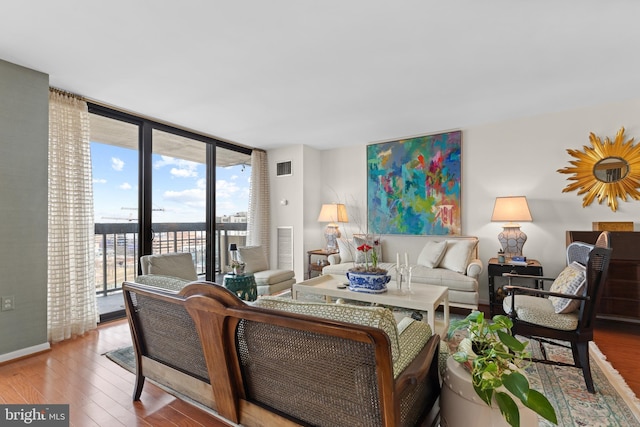 living area with a wall of windows, wood finished floors, visible vents, and baseboards