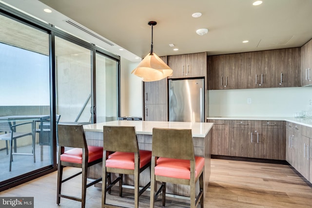 kitchen featuring a breakfast bar, light countertops, freestanding refrigerator, a kitchen island, and light wood-type flooring