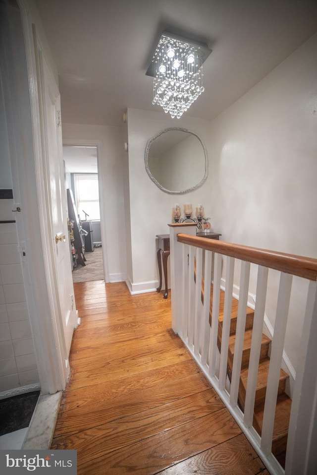 corridor featuring light wood-style floors, baseboards, stairway, and a chandelier