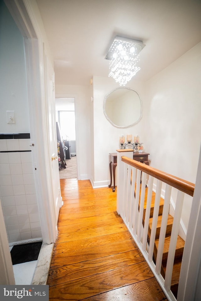 hall featuring light wood-style floors, tile walls, and an inviting chandelier