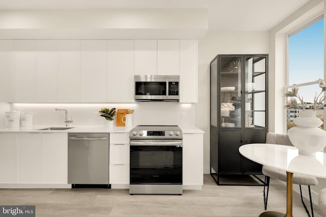 kitchen featuring sink, stainless steel appliances, white cabinetry, and light wood-type flooring