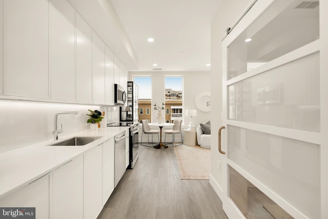 kitchen with sink, white cabinets, stainless steel appliances, and light hardwood / wood-style floors