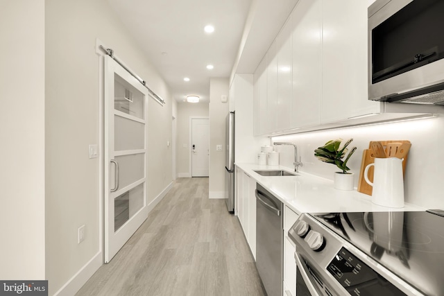 kitchen with appliances with stainless steel finishes, light wood-type flooring, a barn door, sink, and white cabinetry