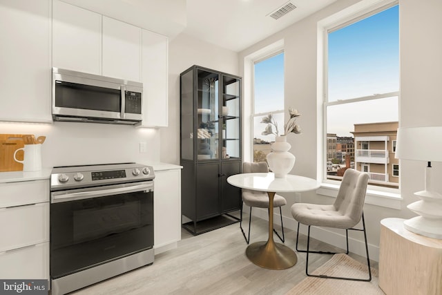 kitchen with appliances with stainless steel finishes, white cabinets, and light hardwood / wood-style flooring